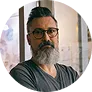 Man with glasses and a beard wearing a dark gray shirt standing indoors.
