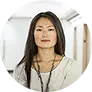 Confident woman with long dark hair wearing a white top standing in a modern office hallway.