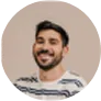 Smiling man with short dark hair and beard wearing a striped shirt on beige background.