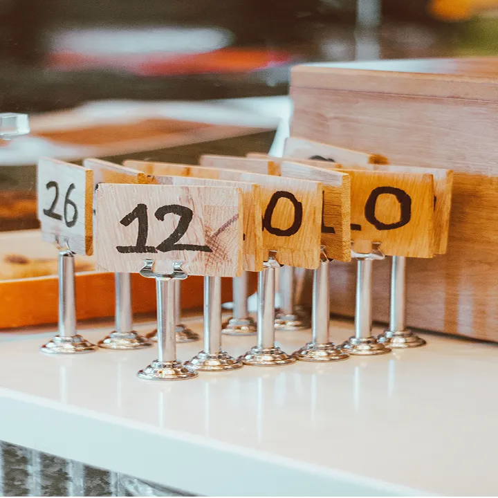 Row of wooden table number signs with metal bases on a white surface, showing the numbers 26, 12, and 0 among others.