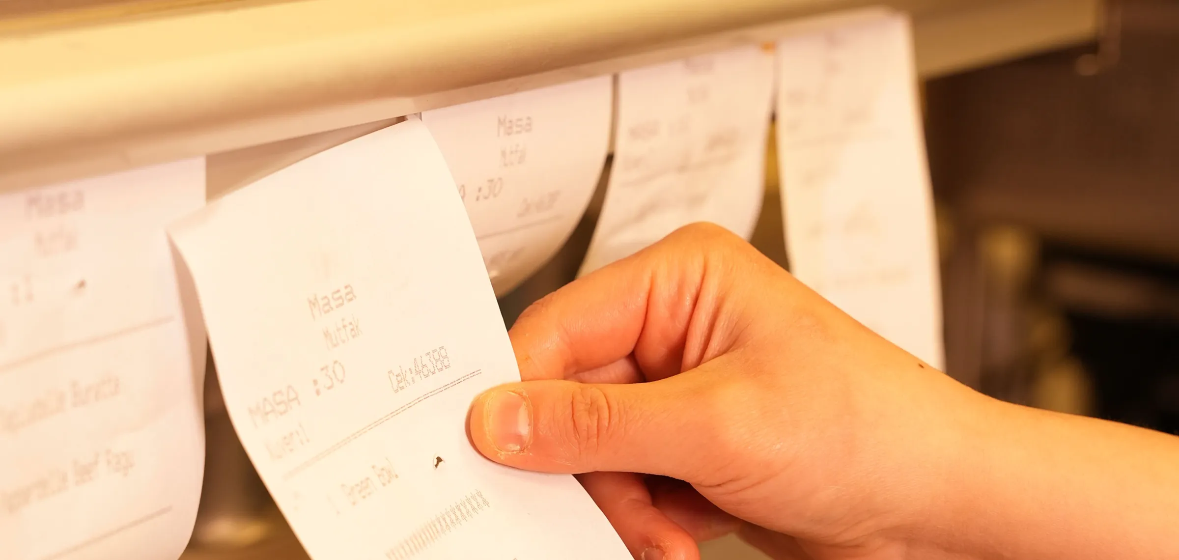 Hand holding and retrieving a printed receipt or order ticket from a rack with similar hanging tickets.