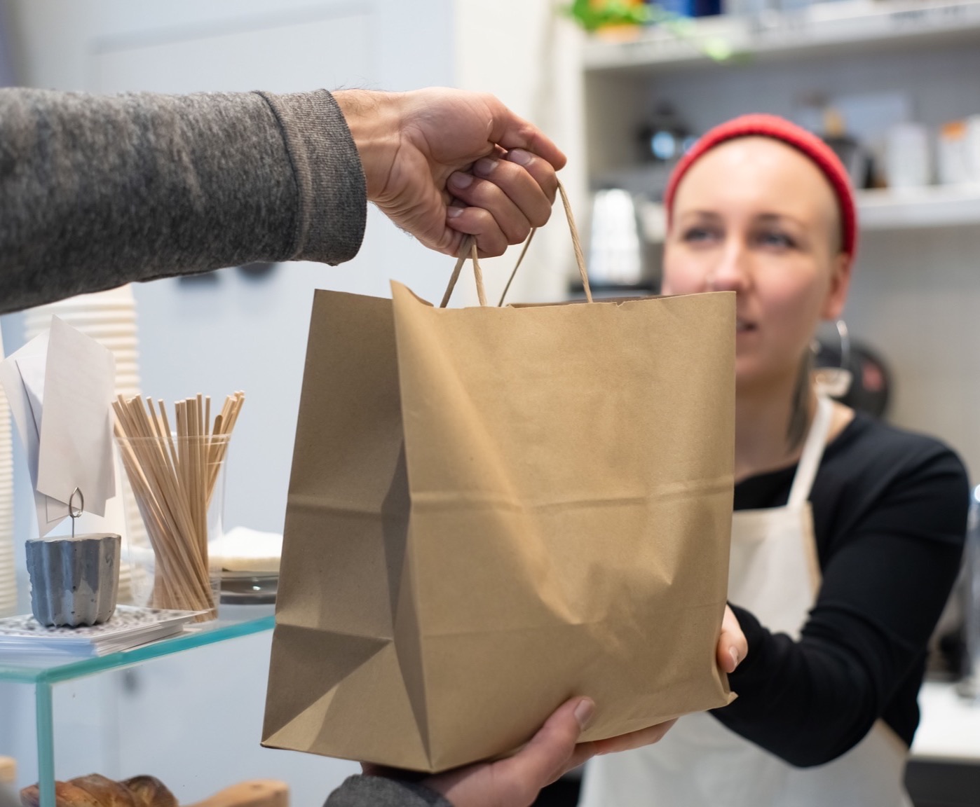 Une employée en tablier tend un sac de commande à emporter à un client