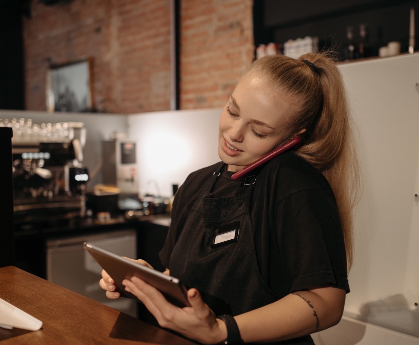 Une serveuse répond au téléphone au comptoir, une tablette à la main, pendant le service